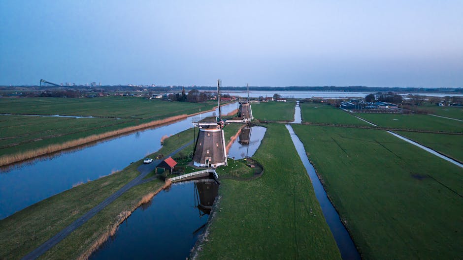 Captivating aerial view of iconic Dutch windmills surrounded by lush green fields and canals at dusk.